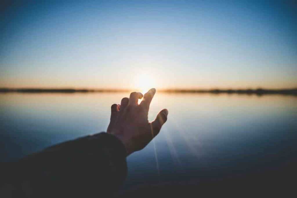 Hand reaching toward the rising sun over calm water, representing hope, renewal, and emotional healing with EMDR therapy.