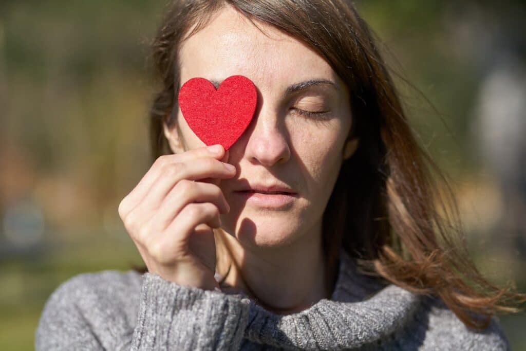 Woman holding red heart over eye symbolizing self-love and overcoming comparison