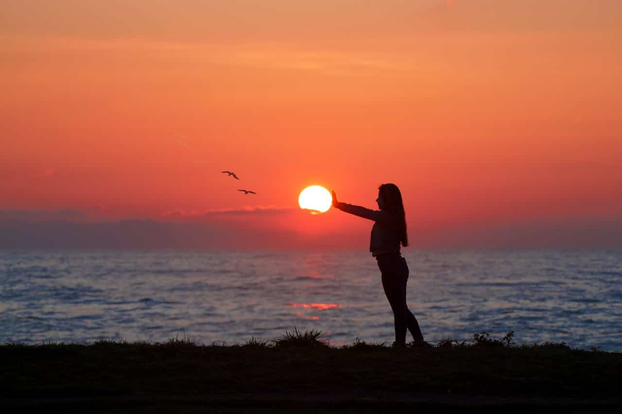 A person standing by the ocean at sunset, appearing to hold the sun in their hands, symbolizing focus and deep emotional work.