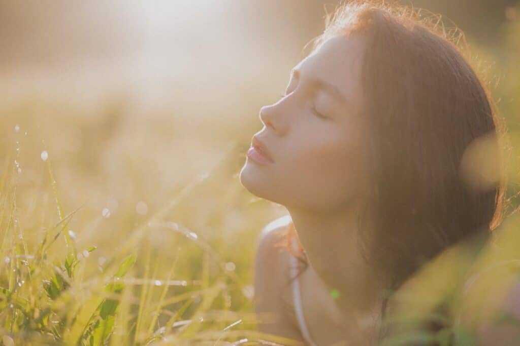 Woman resting peacefully in sunlight with eyes closed, representing inner calm and emotional release.
